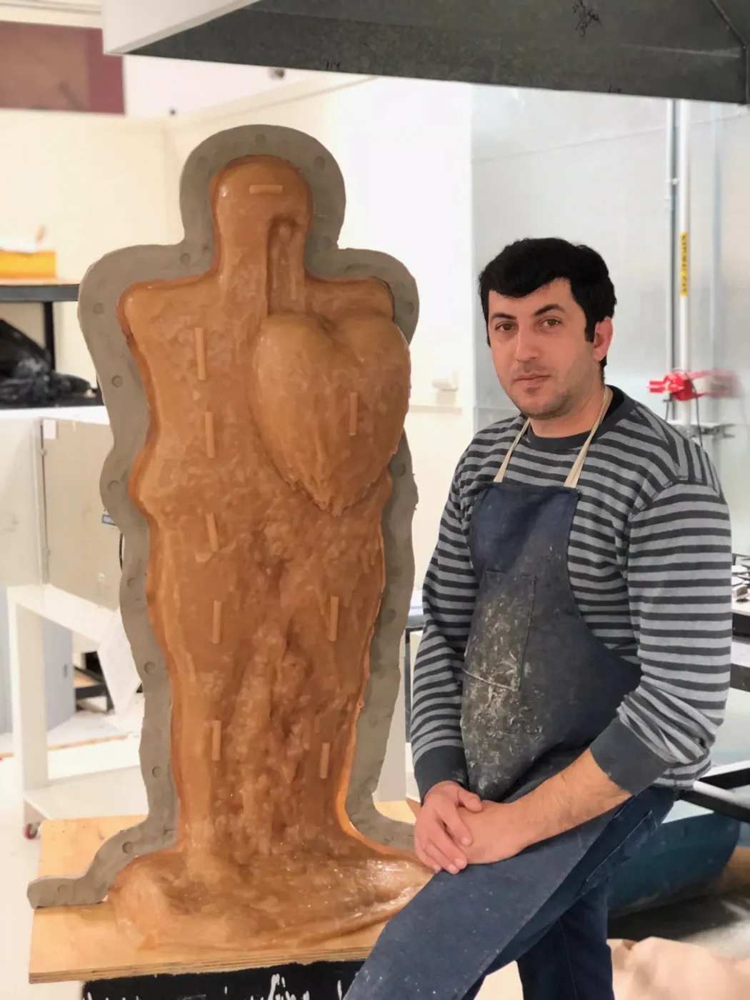 Mishaal Atheer in the studio, seated beside a large figure in its mold